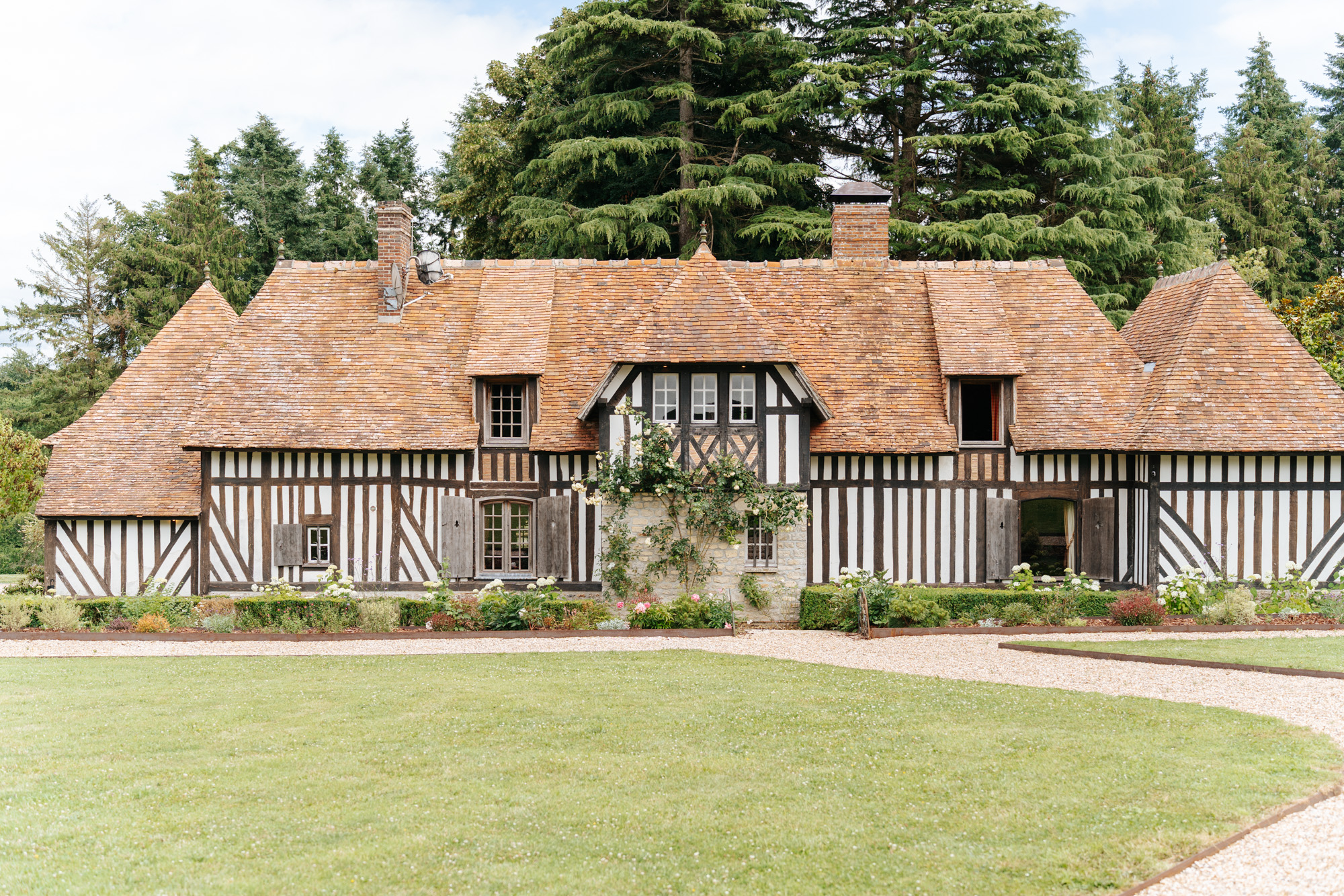 Main façade of the Domaine de Barneville manor house with climbing roses and a lush garden