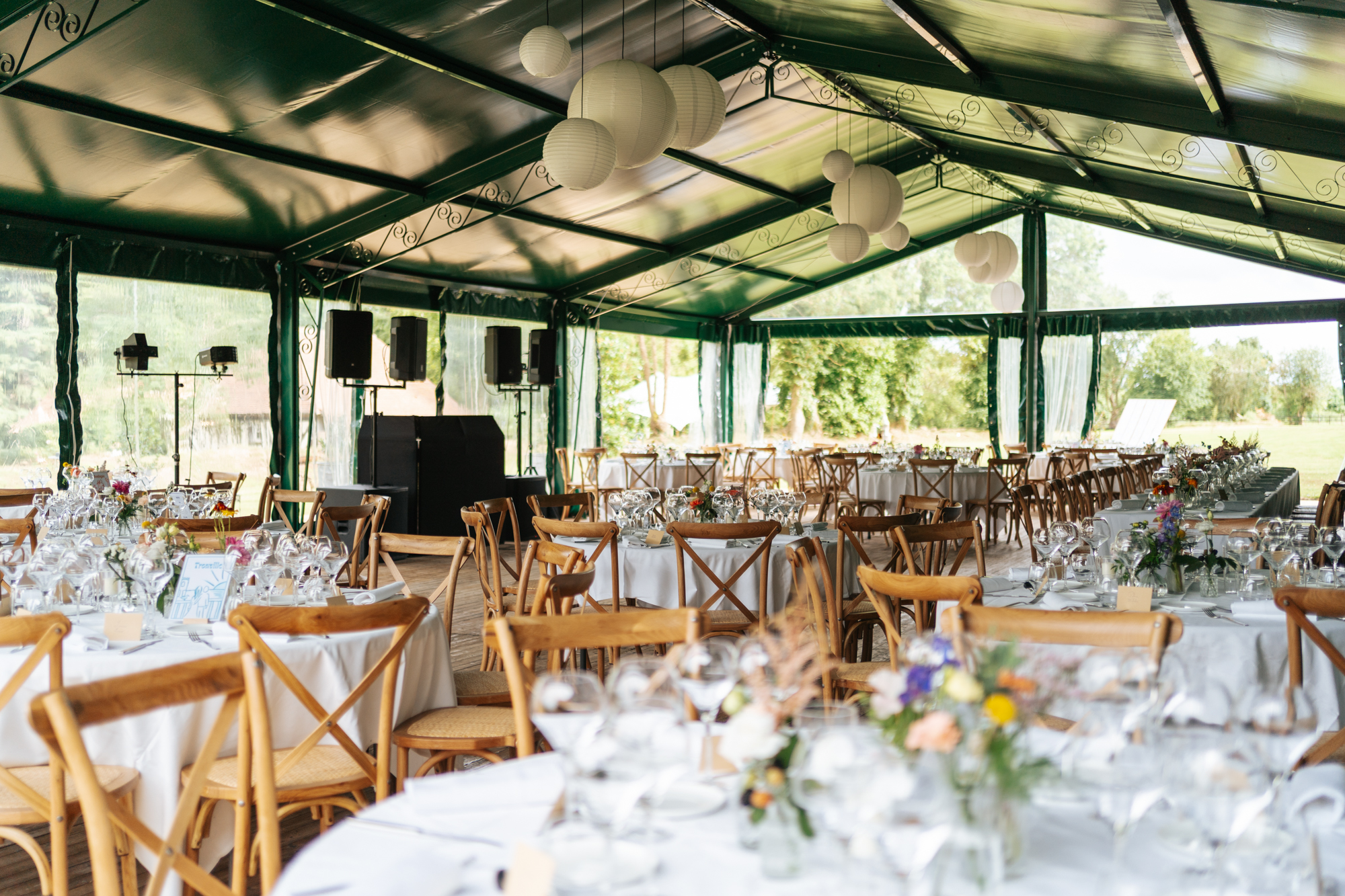 Wedding reception tables inside a large tent with colorful floral centerpieces and wooden chairs at Domaine de Barneville.